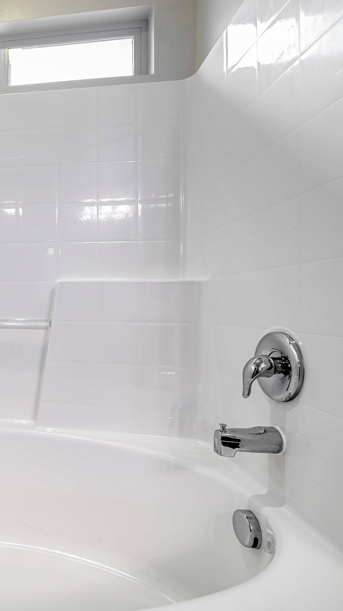 Fitted white oval bathtub set into a tiled alcove